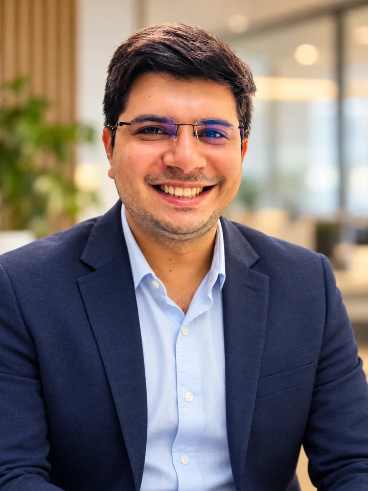 Sanu Siddharth smiling, wearing glasses, a navy blazer, and a light blue shirt